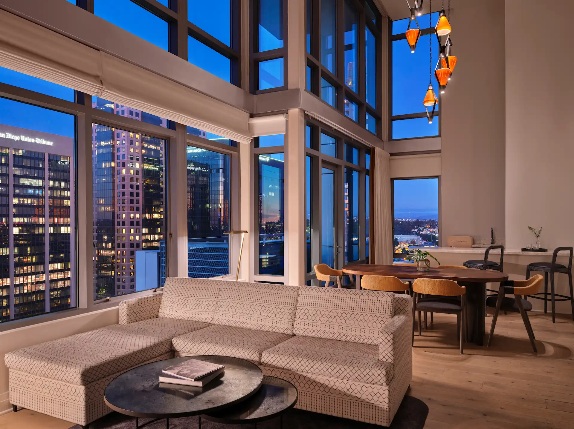 Dining and living area of the 2 Bedroom Presidential Suite, featuring large windows with city views at sunset